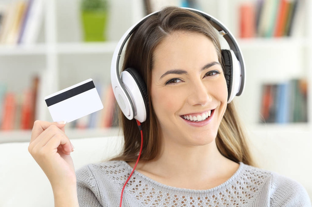 Chica escuchando música y mostrando la tarjeta de crédito en blanco
 - Foto, imagen