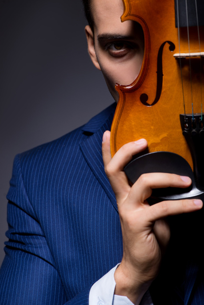 Молода людина грає на скрипці в темній кімнаті
 - Фото, зображення