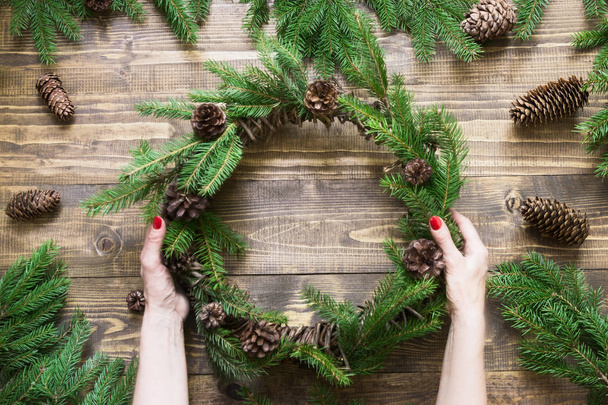 Christmas wreath with fir branches on wooden board in female hand. Top view. - Photo, Image