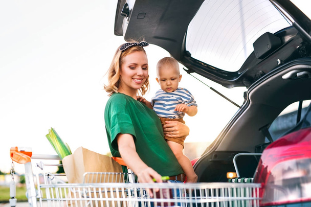 Mother with baby boy putting shopping into back of car. - Photo, image