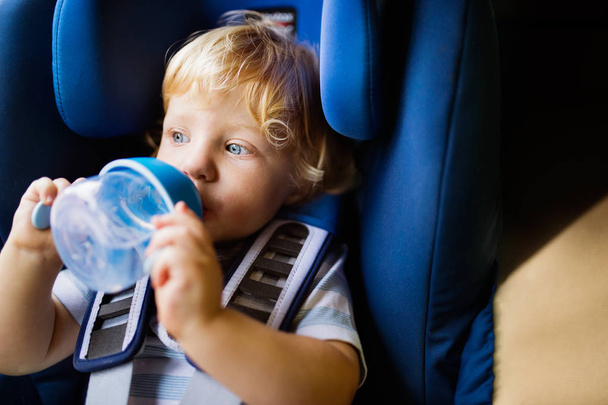 Little boy sitting in the car seat in the car, drinking. - Photo, Image