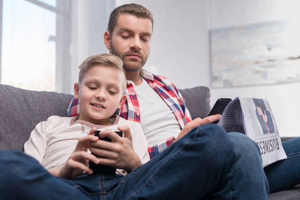 padre e hijo con periódico y smartphone
 - Foto, imagen