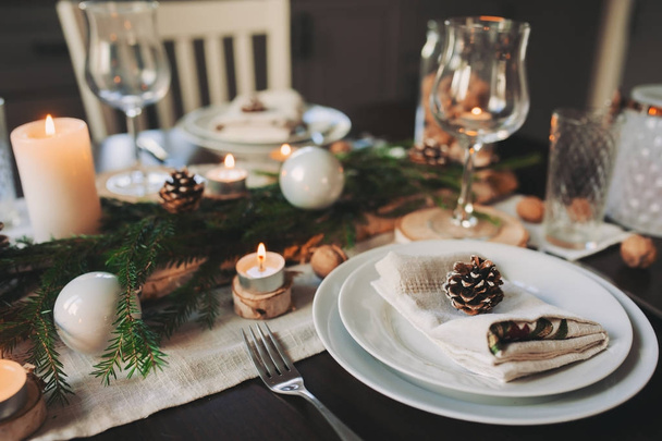 Festive Christmas and New Year table setting in scandinavian style with rustic handmade details in natural and white tones. Dining place decorated with pine cones, branches and candles - Фото, изображение