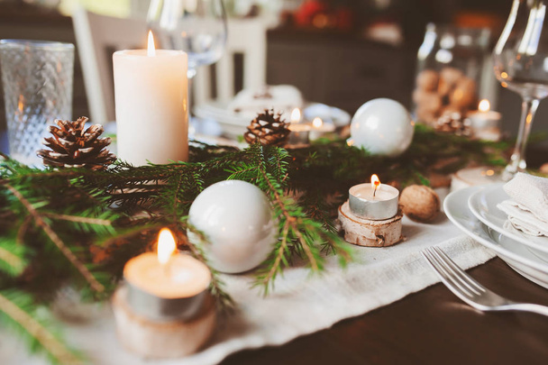 Festive Christmas and New Year table setting in scandinavian style with rustic handmade details in natural and white tones. Dining place decorated with pine cones, branches and candles - Fotoğraf, Görsel