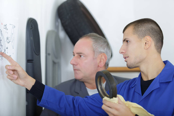 two mechanics questioning themselves about car part - Foto, afbeelding