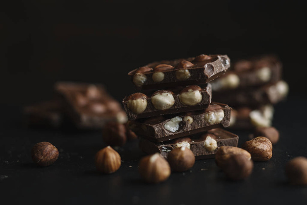 Chocolate bar pieces and nuts on dark slate background with copy space. Chocolate background. Top view. Toned - Zdjęcie, obraz