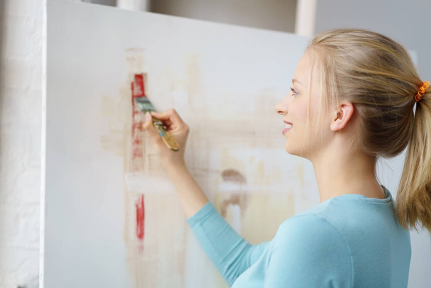 Young blonde woman painting picture in atelier - Фото, зображення