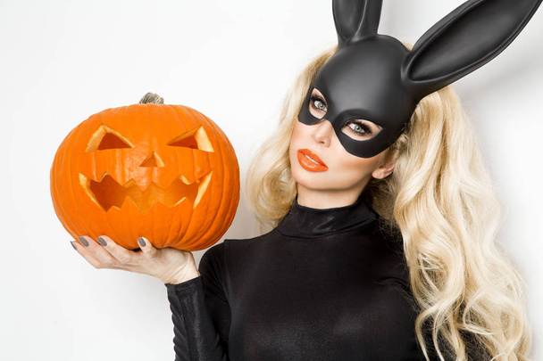Красивая молодая женщина в костюме кролика Хэллоуина, стоящая рядом с пасхальной корзиной и держащая тыкву
 - Фото, изображение