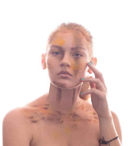 Attractive young woman with face painted to yellow and brown. Looks to camera. Touch her face by hand fingers. Light background. - Φωτογραφία, εικόνα