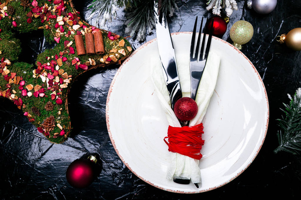 Vánoční prostírání stolu. Svátky na pozadí. Bílá deska, nůž a vidlička s vánoční výzdobou na černém stole. Pohled shora. - Fotografie, Obrázek