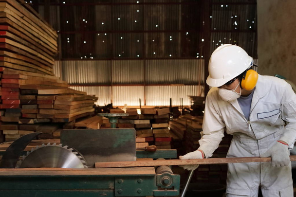 Zawodowej młodych pracowników w biały uniform i bezpieczeństwa cięcia kawałek drewna na stół piły w fabryce stolarki. Vintage zdjęcie stonowanych - Zdjęcie, obraz