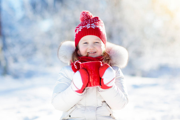 Παιδί πίνοντας ζεστή σοκολάτα στο χειμερινό πάρκο. Τα παιδιά στο χιόνι σε Chr - Φωτογραφία, εικόνα
