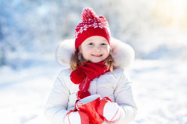 Ребенок пьет горячий шоколад в зимнем парке. Дети в снегу на Chr
 - Фото, изображение