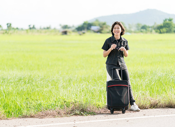 Mujer con equipaje haciendo autostop a lo largo de un camino
 - Foto, Imagen