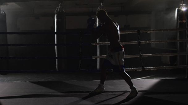 Kickboksen vechter Shadow boksen in de ring. De atleet vecht met zijn schaduw. Jonge bokser in opleiding gooien van een punch met bandages op zijn vuisten als hij werkt in de ring - Foto, afbeelding