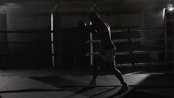 Kickbox-Kämpfer Schattenboxen im Ring. kämpft der Athlet mit seinem Schatten. junger Boxer im Training, der einen Schlag mit Bandagen auf die Fäuste wirft, während er im Ring trainiert - Foto, Bild