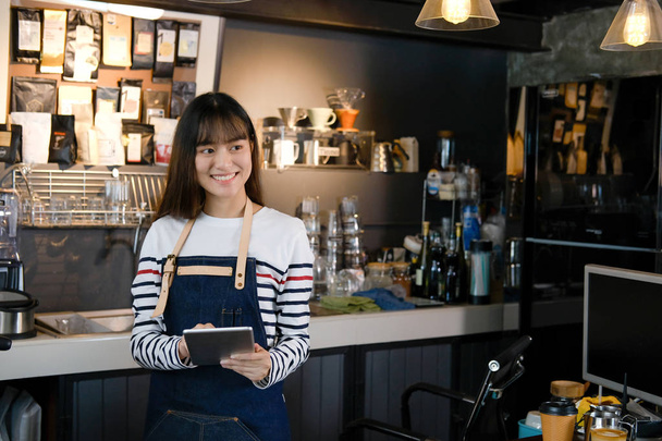 Portrait of smiling asian barista holding digital tablet at coun - Photo, Image