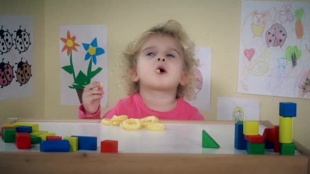 Dziewczynka jeść pyszne kukurydzy okręgi na jej stole pokój - Materiał filmowy, wideo