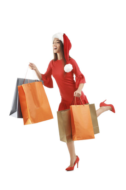 Young woman in Santa hat holding colorful shopping bags on white background. Boxing day concept - Foto, Bild