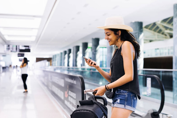 Nő a smartphone repülőtéren. Fiatal utazók ellenőrzése, nevetve, mosolyogva mobiltelefon app a pályaudvar. Nyaralás a turisztikai. - Fotó, kép