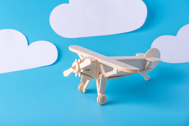 Avião de brinquedo de madeira em um fundo de céu azul com nuvens de papel. Conceito de viagem e companhias aéreas
 - Foto, Imagem
