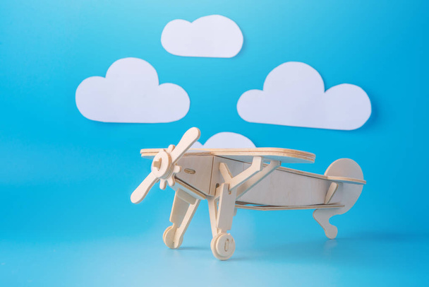 Avião de brinquedo de madeira em um fundo de céu azul com nuvens de papel. Conceito de viagem e companhias aéreas
 - Foto, Imagem