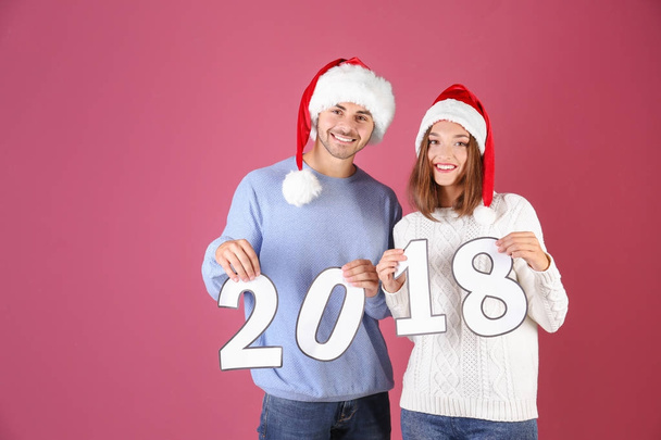 Young couple with paper figures 2018 on color background. Christmas celebration concept - Фото, изображение