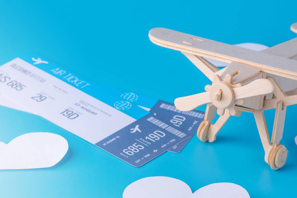 Avião de brinquedo de madeira e bilhetes em um fundo de céu azul com nuvens de papel. Conceito de viagem e companhias aéreas
 - Foto, Imagem