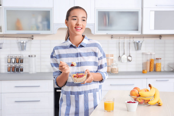 Young woman in pajamas eating oatmeal in kitchen - Фото, изображение