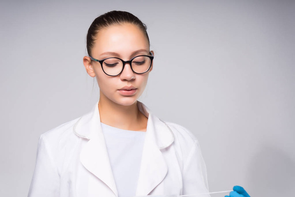 young successful girl doctor in glasses, white medical dressing gown looks down - Foto, imagen