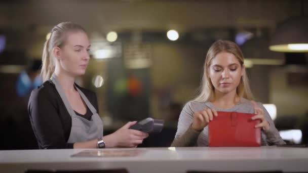 A young and pretty woman takes out a bank card from her handbag in order to pay the bill in the restaurant through the payment terminal - Filmmaterial, Video