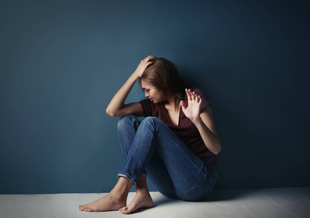 Battered young woman sitting near blue wall - Fotoğraf, Görsel