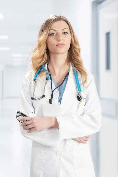 Жінка-лікар в білому хірургічному пальто з стетоскопом стоїть
 - Фото, зображення