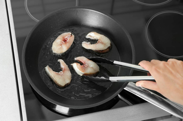 Woman frying fish steaks on pan in kitchen - Foto, afbeelding