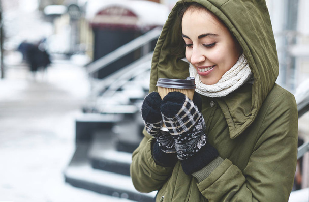 Portrait of young woman drinking tea outdoors at winter street. - Photo, image