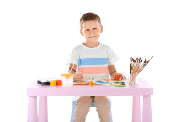 Talented boy painting while sitting at table against white background - Фото, изображение