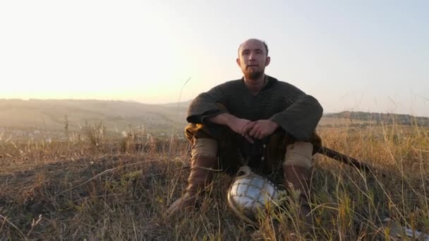 Porträt eines Wikingers, der mit Kettenhemd und Helm auf dem Gras sitzt - Filmmaterial, Video