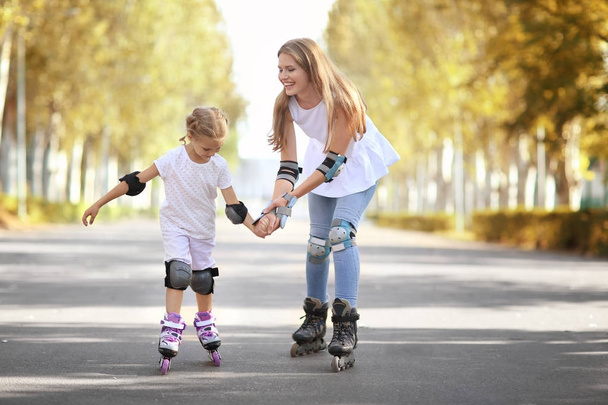 Mother with daughter rollerskating in park - Фото, изображение