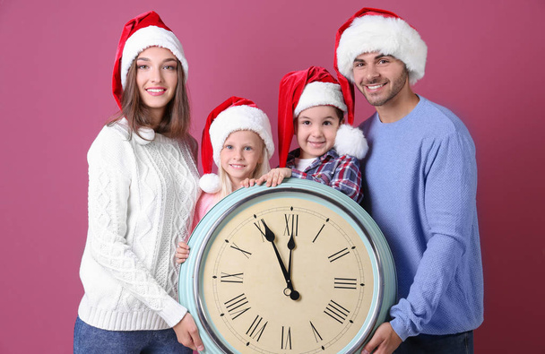 Happy family in Santa hats with clock on color background. Christmas countdown concept - Foto, imagen