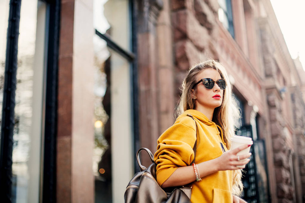 Outdoor waist up portrait of young beautiful woman with long hair. Model wearing stylish sunglasses, clothes, holding bag. City lifestyle. - Φωτογραφία, εικόνα