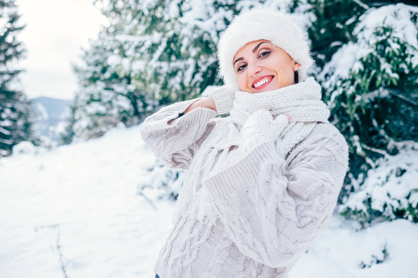 Lächelnde Frau in kuscheligem Strickpullover und Pelzmütze auf winterlicher Waldlichtung - Foto, Bild