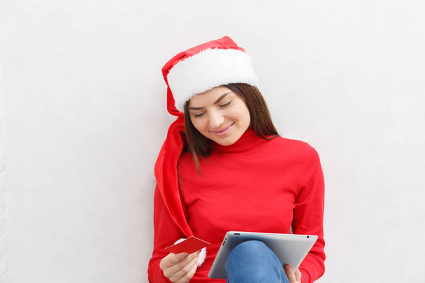 A girl in Christmas clothes is sitting on the floor with a tablet - Fotografie, Obrázek