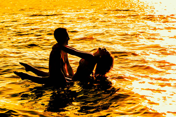 Two young adult lovers standing in water at  sunset  - 写真・画像