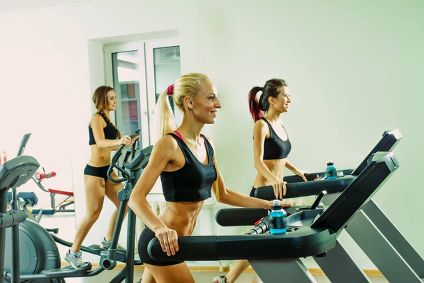  young sporty women running  on treadmills  in the gym - Fotó, kép