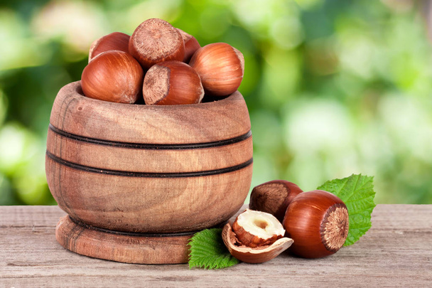 Hazelnuts with leaves in a wooden bowl on a wooden table with blurred garden background - Photo, Image