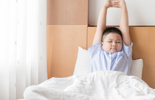 obese fat boy wakes up and stretching on bed. - Фото, изображение