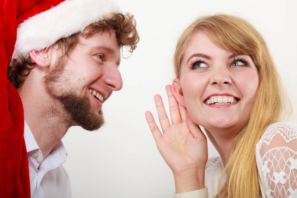 Man in santa hat whispering to woman ear. - Фото, зображення