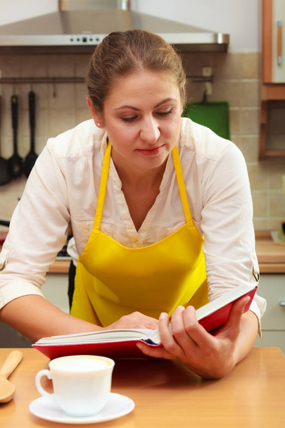 Housewife woman reading cookbook in kitchen. - Zdjęcie, obraz