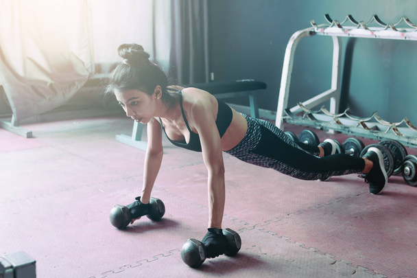 Young asian woman doing push-ups on dumbbell in a gym. - Foto, immagini