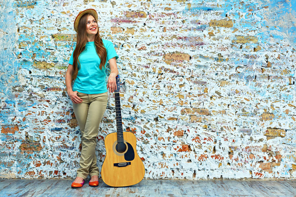 street photo of smiling young woman with guitar standing against brick wall  - Fotó, kép